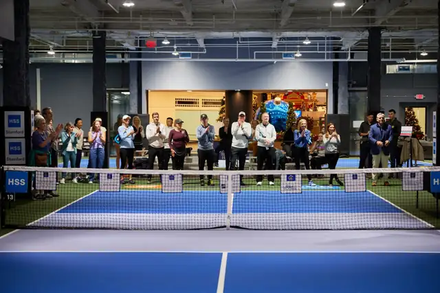 A crowd of spectators stands along the far side of a blue court, applauding behind the net.