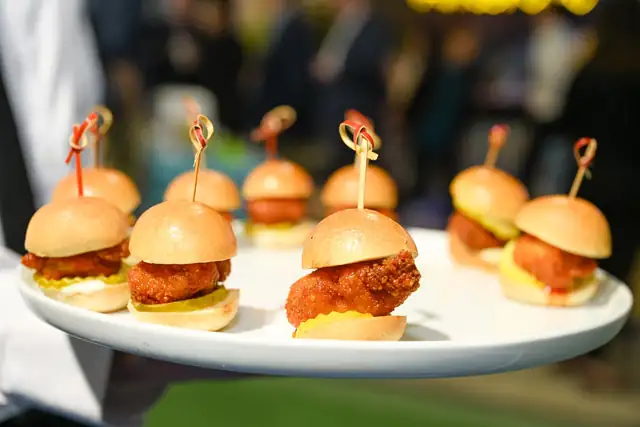 A white platter of fried chicken sliders, each held together with a wooden skewer.