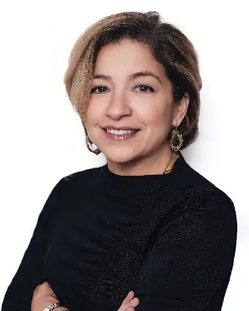 Mia Schipani, smiling with arms folded, in a black top against a white background.