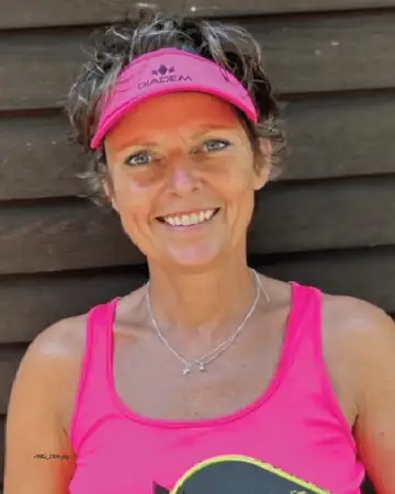 Pernille Halbro, smiling, in a pink visor and pink tank top, in front of a dark wood wall.